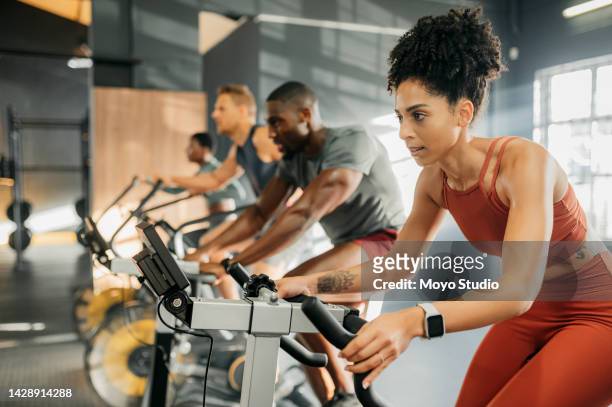 a black woman with group on exercise bike, cycling at gym to lose weight and improve cardiovascular fitness health. a bicycle is the best activity for cardio, healthy fat loss and training for sports - group gym class bildbanksfoton och bilder