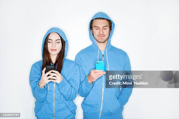 hip young couple in matching hoodies texting - hood clothing stock pictures, royalty-free photos & images