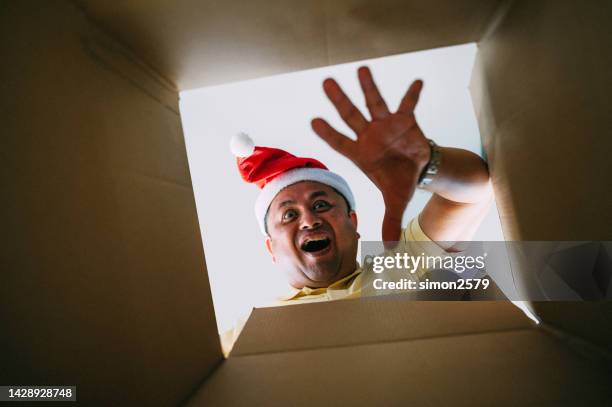 excited asian man wearing santa hat unpacking christmas gift. - unwrapped stock pictures, royalty-free photos & images