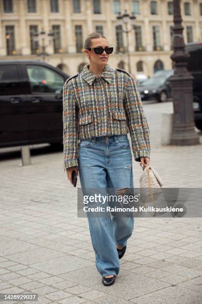 Guest wearing black sunglasses, a beige with green, orange and blue checkered jacket, blue denim ripped large pants, black shiny leather ballerinas...