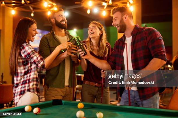 playing game of pool and drinking beer with friends in local pool hall - billiard ball game stockfoto's en -beelden