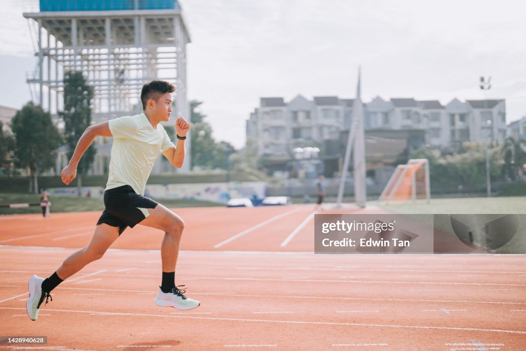 Joven atleta asiático chino entrenando en la pista de atletismo por la mañana en el estadio de atletismo