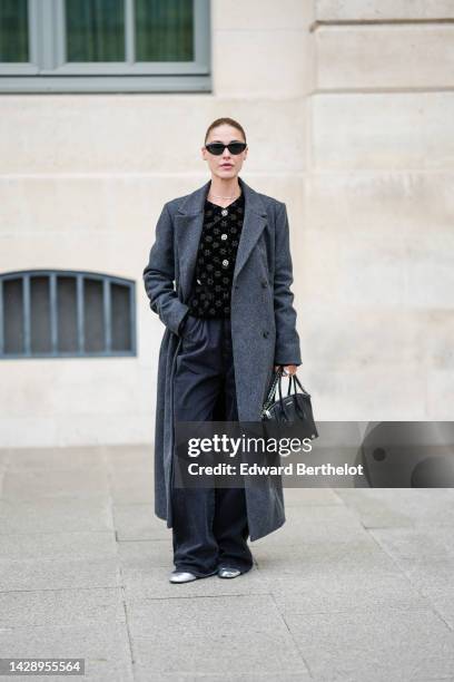 Sophia Roe wears black sunglasses, a silver necklace, a black velvet with embroidered white flower pattern / crystal buttons cardigan, a dark gray...