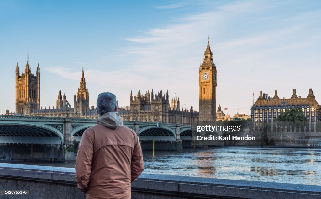 A man looks at Big Ben and Westminster Bridge in London at sunrise