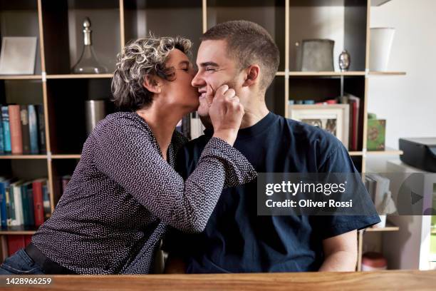 affectionate mature woman with adult son at home - cheek kiss stock pictures, royalty-free photos & images