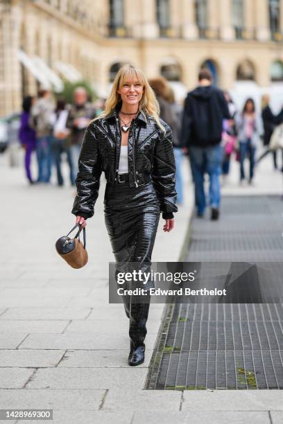 Jeanette Madsen wears black with silver heart pendant necklace, a black shiny varnished leather crocodile print pattern cropped jacket, a matching...