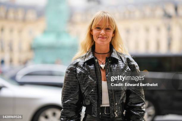 Jeanette Madsen wears black with silver heart pendant necklace, a black shiny varnished leather crocodile print pattern cropped jacket, a matching...