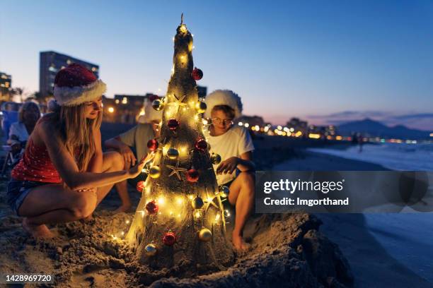 mehrgenerationen-familie genießt abend am strand mit sandweihnachtsbaum - christmas family tree stock-fotos und bilder