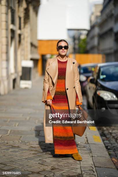 Guest wears black sunglasses from Celine, gold earrings, a gold chain diamond pendant necklace, a red / orange / black braided wool long / flared...