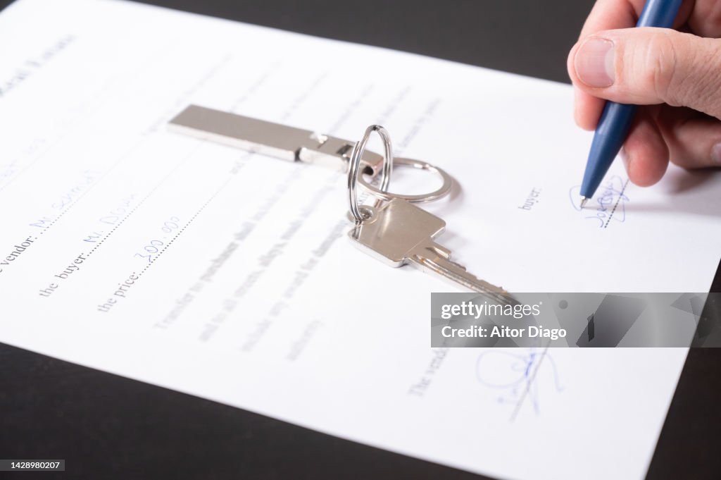 Concept buying / selling a home. The buyer firms the contract for buying a home. There is a key on the table.