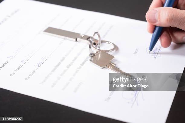 concept buying / selling a home. the buyer firms the contract for buying a home. there is a key on the table. - sold single word - fotografias e filmes do acervo