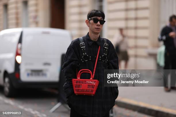 Guest is seen wearing a black sunglasses, black checked oversize shirt, a red Balenciaga basket bag, black pleated long skirt, grey socks and yellow...