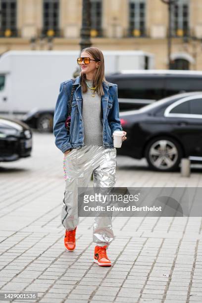 Guest wears orange sunglasses, a gray wool pullover, a blue denim jacket, a white with purple / orange / green print pattern shoulder bag from...
