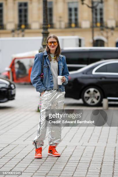 Guest wears orange sunglasses, a gray wool pullover, a blue denim jacket, a white with purple / orange / green print pattern shoulder bag from...