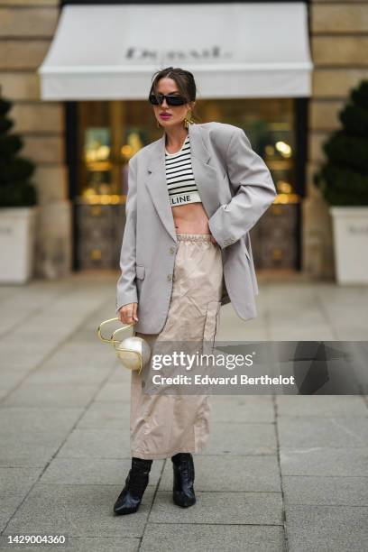 Guest wears black sunglasses, gold fringed pendant large earrings, a white latte and black striped print pattern cropped bra from Celine, a pale gray...