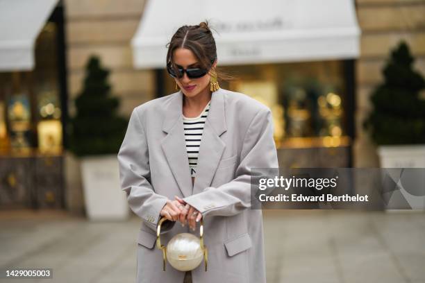 Guest wears black sunglasses, gold fringed pendant large earrings, a white latte and black striped print pattern cropped bra from Celine, a pale gray...