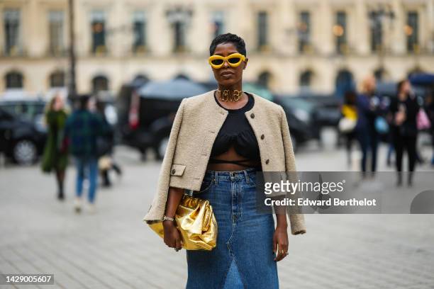 Guest wears yellow sunglasses from Loewe, a gold large necklace with Love large details, a black laces waist cropped top from Jacquemus, a beige...