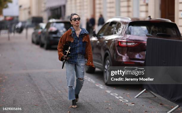 Guest is seen wearing black sunglasses, silver necklaces, blue checked shirt jacket with brown suede leather details, black leather bag and a light...