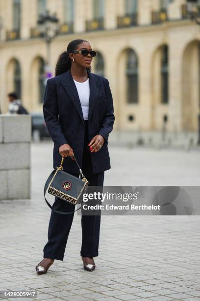 Guest wears black sunglasses from Celine, gold earrings, a white ripped tank-top, a black striped print pattern blazer jacket, matching black striped...