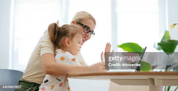 mother and her daughter talking on a video call on digital tablet together at home - woman blond looking left window stockfoto's en -beelden