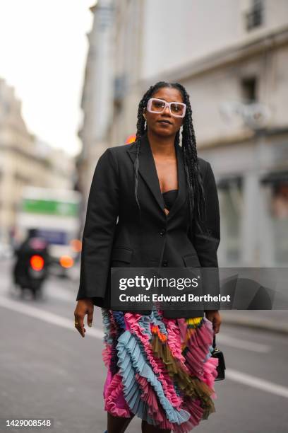 Guest wears pale purple square sunglasses, earrings, a black oversized blazer jacket, a black bra, a blue / pink / brown / yellow ruffled pattern...