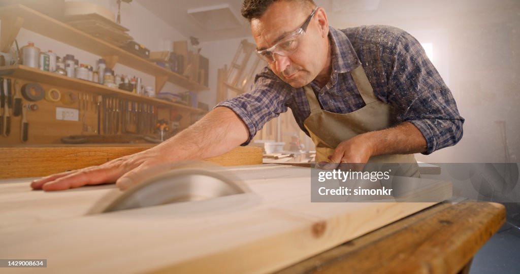 Male carpenter cutting wooden plank in workshop