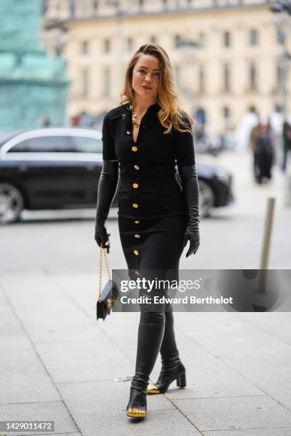 Guest wears a gold large necklace, a black short sleeves / with gold buttons short dress from Schiaparelli, black shiny leather high gloves, a black...