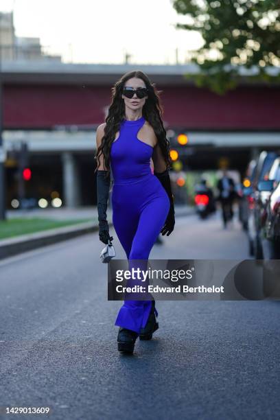Guest wears black butterfly sunglasses, neon purple halter-neck / flared jumpsuit , black high gloves, a silver shiny sequined Hourglass micro...