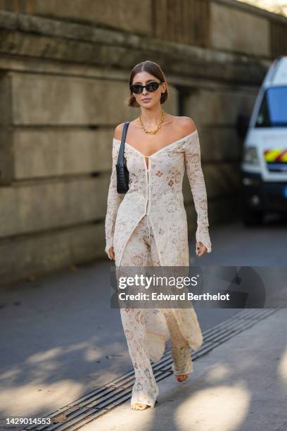 Guest wears black sunglasses, a gold large chain necklace, a black shiny leather crocodile print pattern shoulder bag, a white latte lace print...