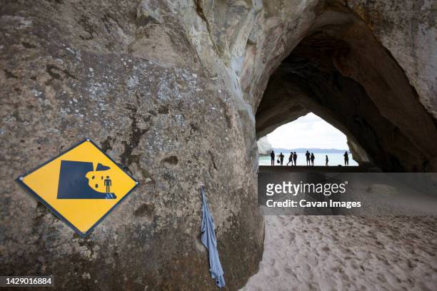 warning sign in front of cave tunnel rock, new zealand - cathedral cove stock pictures, royalty-free photos & images