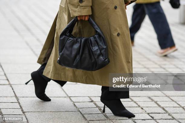 Guest wears a khaki long trench coat, a black shiny leather handbag, black pants, black suede pointed heels ankle shoes , outside Chloe, during Paris...