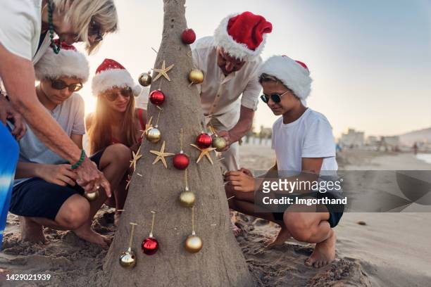 mehrgenerationen-familie schmückt sandweihnachtsbaum an sommerweihnachten - christmas family tree stock-fotos und bilder