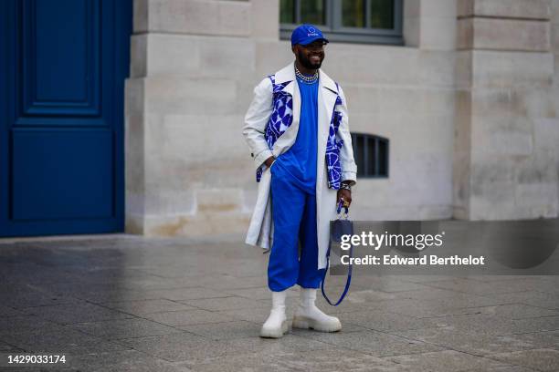 Guest wears a royal blue with white "etude" slogan and stars embroidered pattern cap, silver large chain necklaces, a royal blue oversized t-shirt,...