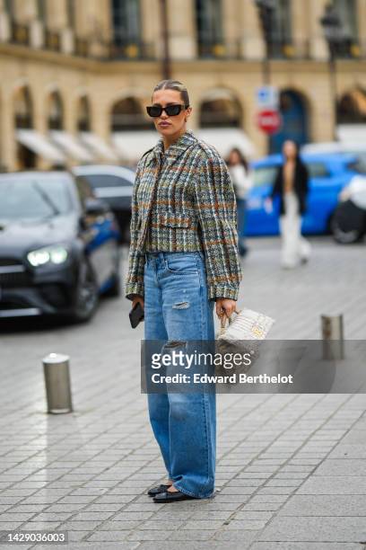 Guest wears black sunglasses, a beige with green / orange / blue checkered print pattern tweed jacket, blue denim ripped large pants, black shiny...