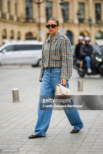 Guest wears black sunglasses, a beige with green / orange / blue checkered print pattern tweed jacket, blue denim ripped large pants, black shiny...