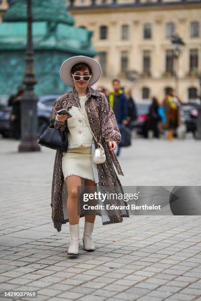 Guest wears a white felt hat, white sunglasses, a beige and black snake print pattern long coat, a white late tweed / fringed / jacket, a matching...