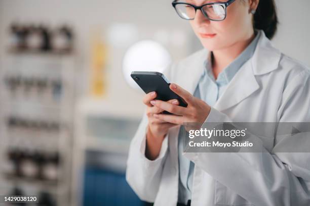 scientist on social media with phone and contact via text while on a break with glasses and a lab coat. young woman chemist or medical researcher typing email and looking relax in medical laboratory - checking phone bildbanksfoton och bilder