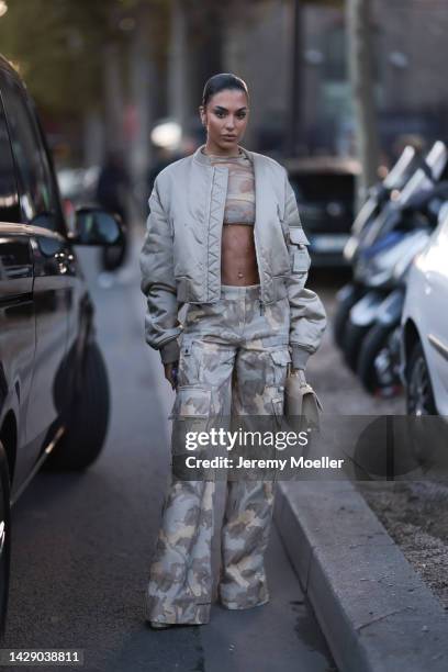 Jessica Aïdi Verratti is seen wearing gold earrings, beige and white latte military print pattern transparent cropped top, matching beige and grey...