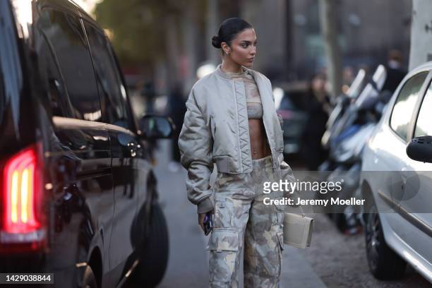 Jessica Aïdi Verratti is seen wearing gold earrings, beige and white latte military print pattern transparent cropped top, matching beige and grey...