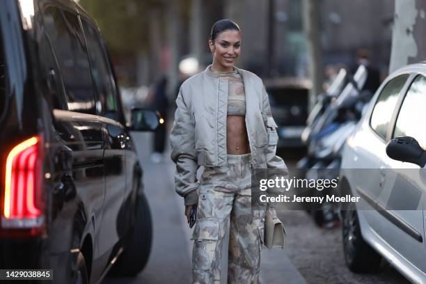 Jessica Aïdi Verratti is seen wearing gold earrings, beige and white latte military print pattern transparent cropped top, matching beige and grey...