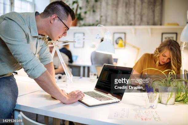 cheerful programmer in shared office working on laptop. coding expert working with colleagues - code 41 bildbanksfoton och bilder