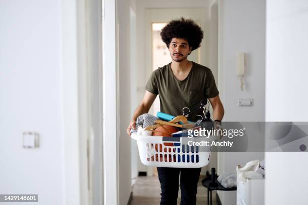 junger männlicher student, der ins wohnheim zieht und auspackt - washing basket stock-fotos und bilder