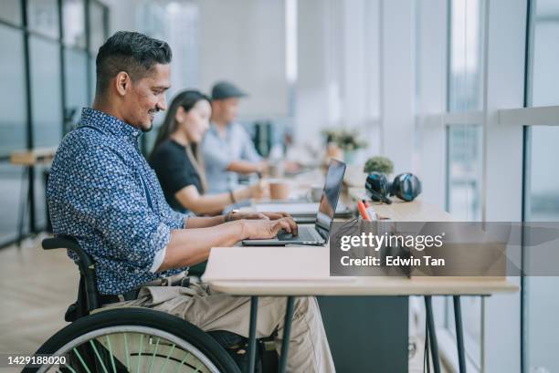 asian indian white collar male worker in wheelchair concentrating working in office beside his colleague - rechten van personen met een handicap stockfoto's en -beelden
