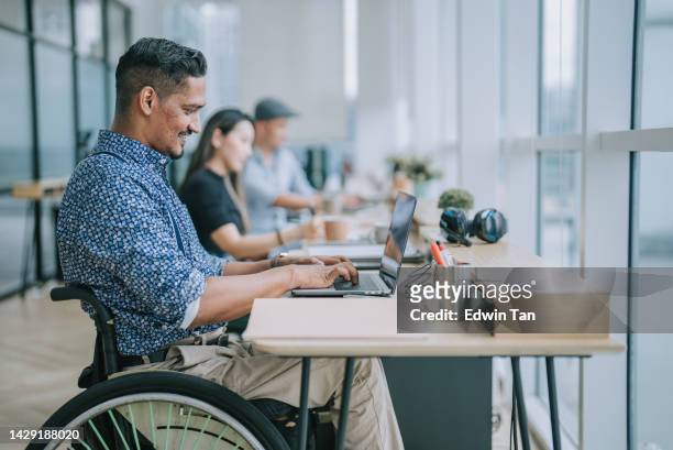 Asian Indian white collar male worker in wheelchair concentrating working in office beside his colleague