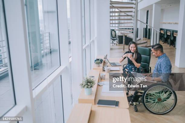 indian white collar male worker in wheelchair  discussion  with  female asian chinese colleague coworking in creative office workstation beside window - business meeting chinese stockfoto's en -beelden