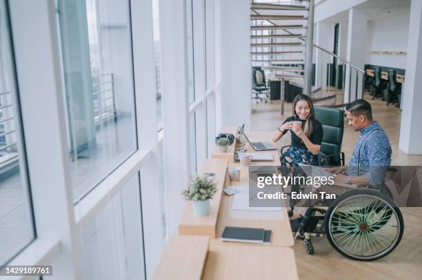 indian white collar male worker in wheelchair  discussion  with  female asian chinese colleague coworking in creative office workstation beside window - disability rights stock pictures, royalty-free photos & images