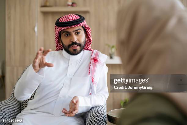 saudi couple enjoying conversation while relaxing at home - kaffiyeh stock pictures, royalty-free photos & images