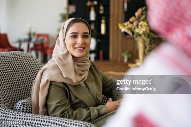 young saudi woman listening and smiling in home living room - headscarf home stockfoto's en -beelden