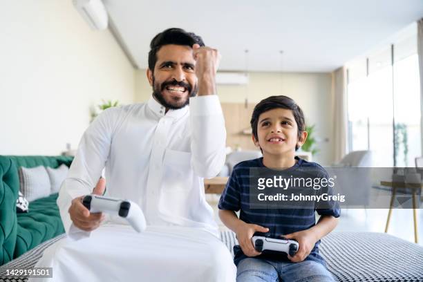 konkurrenzfähiger saudischer vater gewinnt videospiel gegen sohn - saudi youth stock-fotos und bilder