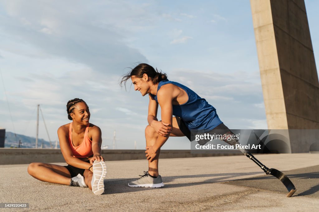 Young disabled man with a leg prosthesis stretching after jogging. Man and woman practicing stretching. Concept of disability.